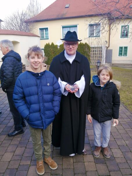 Herr Pfarrer mit zwei Kindern stehen nach der Messe im Freien